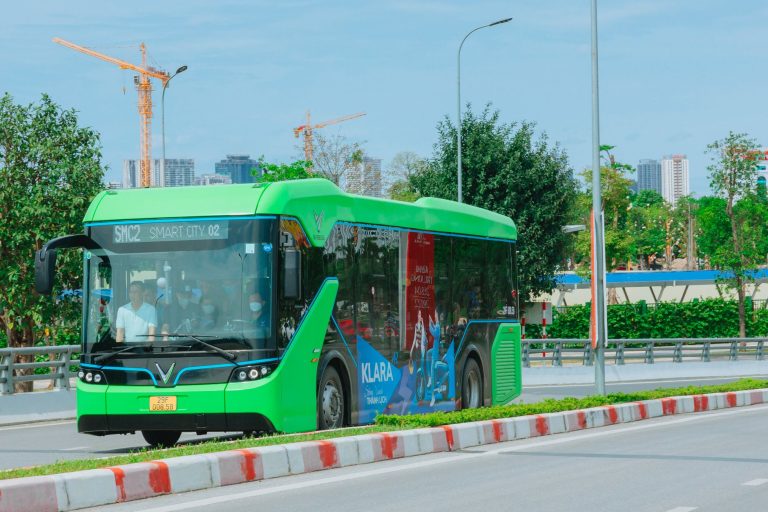 Rio anuncia primeira PPP de ônibus elétricos do Brasil com investimento de R$ 509 milhões Ônibus elétrico verde circula por uma via urbana movimentada, entre prédios e árvores.