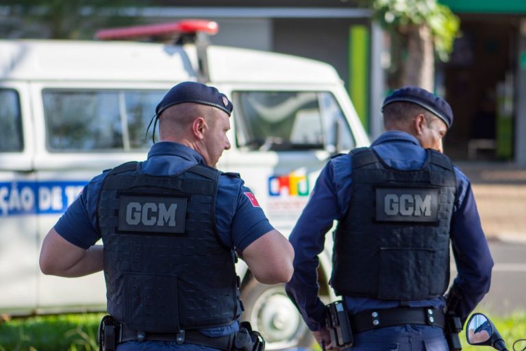 Dois guardas municipais uniformizados patrulham uma rua no Brasil.
