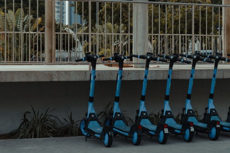 Rio organiza circulação de veículos elétricos e planeja 74 km de motofaixas em 2026 Fileira de patinetes elétricos azuis estacionados ao ar livre.
