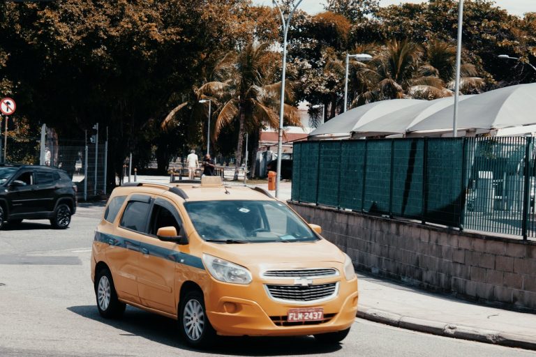 Táxi amarelo circula por uma rua movimentada do Rio de Janeiro em um dia ensolarado.