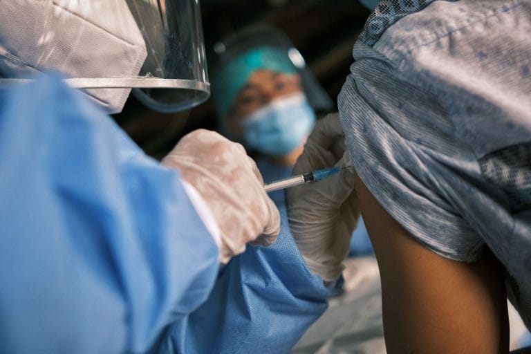 Profissional de saúde aplica uma vacina no braço de um paciente em ambiente clínico.